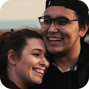 A closeup of a young couple smiling and embracing on a beach.