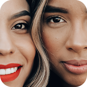 A closeup of two women smiling with their faces next to each other.